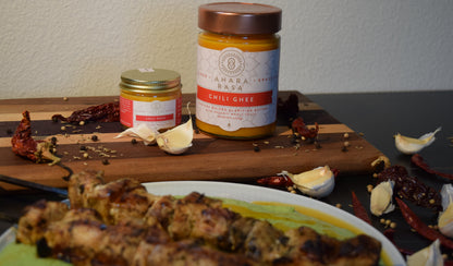 Two jars of Ahara Rasa Chilli Ghee with grilled chicken skewers over a cilantro  puree